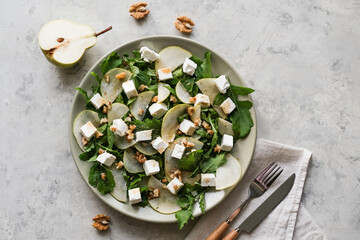Salad with arugula, pear, feta cheese and walnuts. Delicacy salad on a plate on a gray background