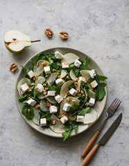 Salad with arugula, pear, feta cheese and walnuts. Delicacy salad on a plate on a gray background