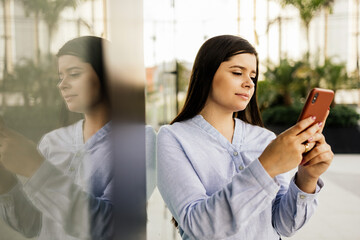 Young businesswoman using smartphone in downtown streets near business buildings