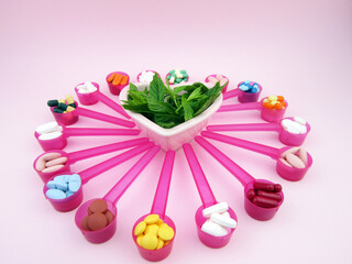    pills, tablets, capsules in pink spoons and plant inside heart in center                      