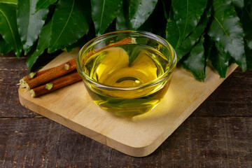 Neem oil in transparent bowl with neem leaf on rustic wooden background.