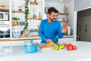 Young sporty man cutting and cooking fresh natural vegetables at kitchen and cooking for healthy lunch. Self care yoga nutritionist having healthy meal after workout.