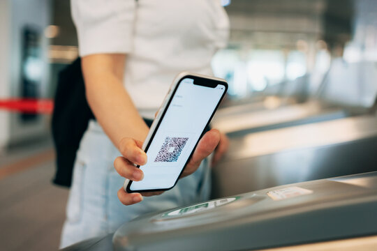 Cropped shot of young Asian woman scanning QR code, checking in at subway station, making a quick and easy contactless payment for subway ticket via smartphone