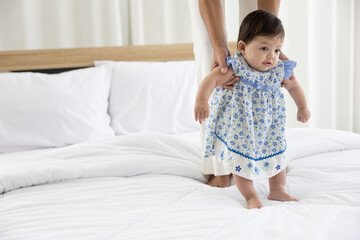 Fototapeta premium baby girl learning to walk and mother or sitter support her on bedroom