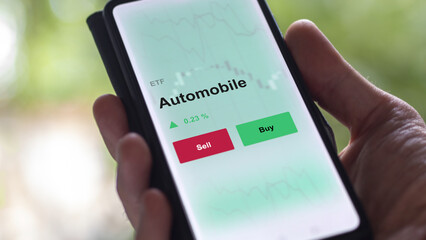An investor's analyzing the automobile etf fund on a screen. A phone shows the prices of car ETFs
