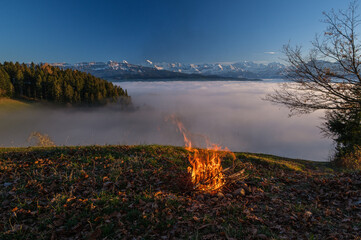 Fototapeta na wymiar Camp fire before sea of fog and swiss alps at sunset