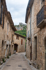 Ruelle étroite avec des maisons médiévales en pierres dans le village de Saint-Guilhem le désert, dans le sud de la France par une journée nuageuse avec des collines escarpées à l'arrière plan.