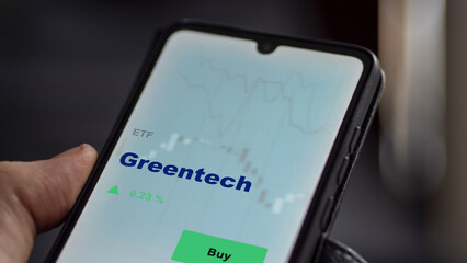 An investor's analyzing the greentech etf fund on a screen. A phone shows the price of green tech
