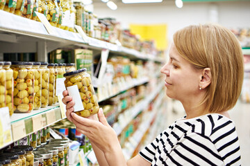 Jar of olives with vegetables in hands woman in store