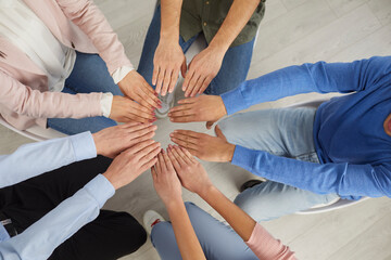 Close up top view of diverse employees sit in circle join hands palms together showing unity. Multiracial people engaged in teambuilding training. Office diversity. Teamwork concept.