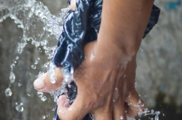 a pair of hands of asian workers rinsing cloth with heavy splashing water in a washing place