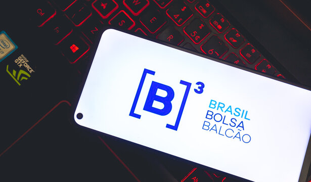 B3 - Bolsa de Valores brasileira. Um celular com a logo da empresa B3 sobre um teclado de notebook gamer com leds vermelhos. Investimento, neg&oacute;cio, preg&atilde;o.