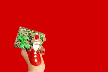 Der Weihnachtsmann hält ein kostbares Geschenk. Der Daumen einer weiblichen Hand ist als lustiger...