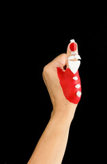 The thumb of a female hand is disguised as a funny Santa Claus with a thump up, isolated on a black...