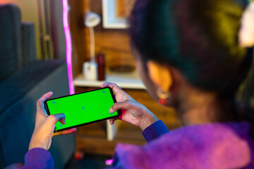 Shoulder shot of teenager girl playing video game on green screen mobile phone at home - concept of enteraiment, gaming addiction and technology
