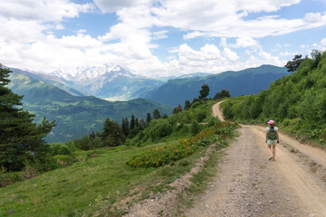 Fototapeta na wymiar Svaneti landscape. Young tourist single traveler woman walking with a backpack. Beautiful Caucasus mountain range near Mestia