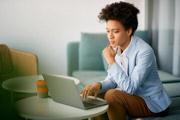 Black female entrepreneur reads an e-mail on laptop in office.