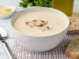 Mushroom soup in a bowl with bread slices and seasonings over wooden table