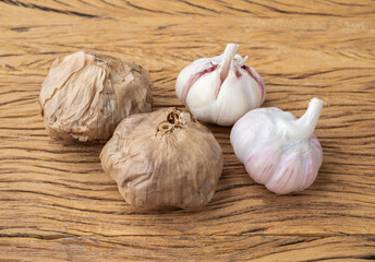 Fermented black garlic and regular garlic bulbs over wooden table