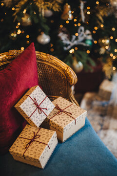 Decorated wrapped present boxes on comfortable armchair near New Year tree. Christmas gifts prepared by unrecognizable person. Beautiful holiday decorated room. Celebration concept
