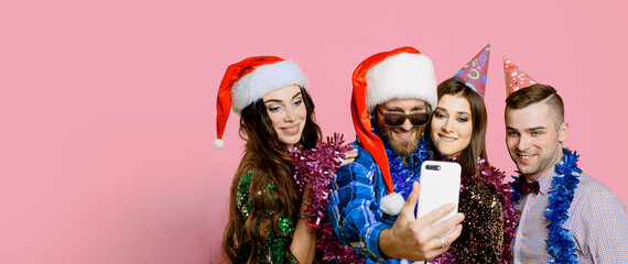 Two girls and two guys 20-25s in holiday hats and santa claus caps and tinsel shoot a video or take...