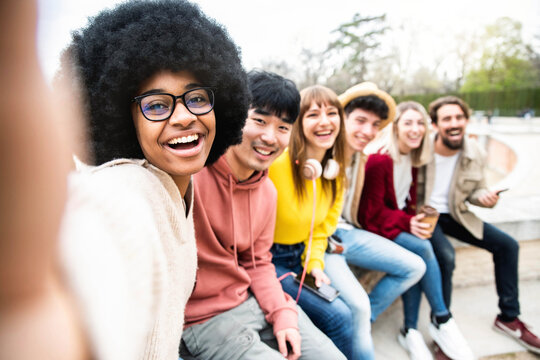 Happy multiracial group of friends taking selfie picture outside - International students having fun together sitting in college campus - Friendship lifestyle concept with guys and girls hanging out