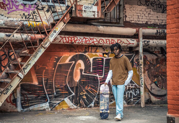 Young handsome stylish black man with natural hair dreadlocks. Afroamerican guy.Stairs,wall painted with graffiti in poor quarter of street art culture city district.African american skateboarder man