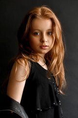 Fototapeta na wymiar Close-up portrait of a adorable little girl with long red hair on black studio background. Fashion kids model