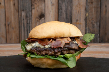 Delicious burger with bread, bacon, mozzarella, blue cheese, meat and spinach leaves, with a wooden...