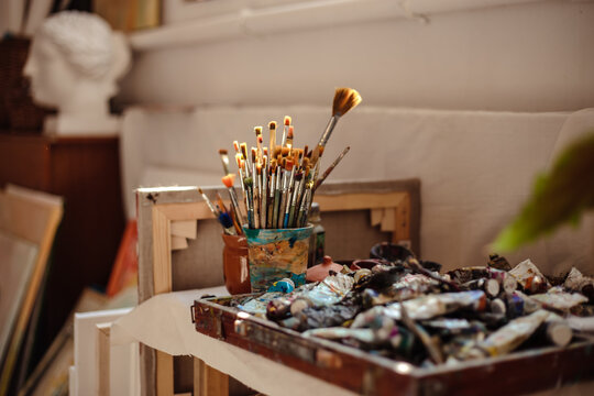 Painting process in artist's workshop, close up photo of brushes and tubes of paint