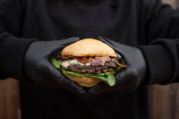 Chef wearing gloves, holding a gourmet burger with bread, bacon, mozzarella, blue cheese, meat and...