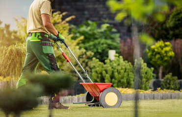Gardener with Push Spreader Fertilizing Residential Grass Lawn - 524508017