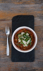 Top view of traditional Hungarian dish, goulash stew with veal and gnocchi, in a black dish on the restaurant wooden table.