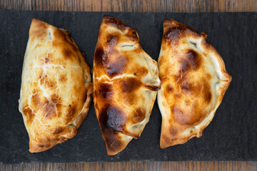 Baked chicken empanadas. Top view of three stuffed pies in a black dish.
