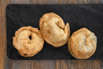 Traditional cheese and ham fried empanadas. Top view of three stuffed pies in a black dish on the wooden table.