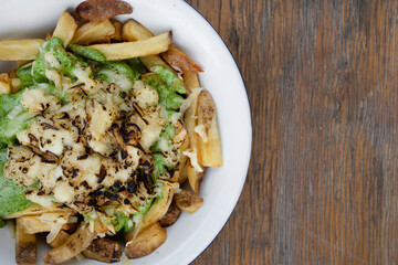 French fries. Top view of a bowl with fried potatoes with spinach cream, mozzarella, cheddar, danvo and blue cheese, in a white bowl on the wooden table. 