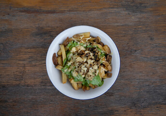 French fries. Top view of a bowl with fried potatoes with spinach cream, mozzarella, cheddar, danvo and blue cheese, in a white bowl on the wooden table. 