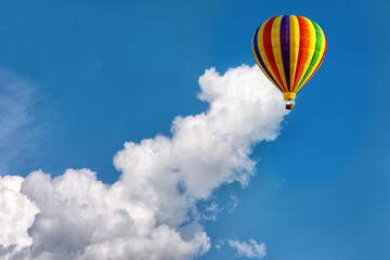Multicolored hot air balloon on background of bright blue cloudy sky.