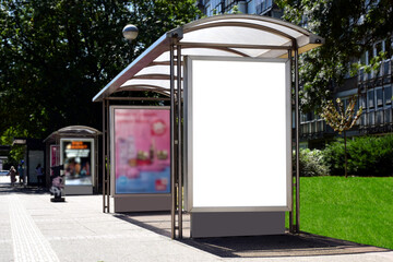 bus shelter with empty white ad panel and light box. urban setting with green park. billboard for...
