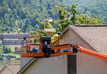 Workman painting the side of a townhouse while standing in an articulating boom lift