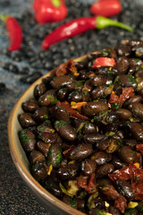 Macro close up of black beans with dried tomatoes and red Cayenne chili peppers in a brown dish.