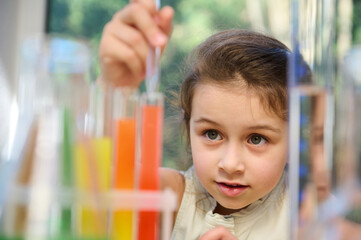 Excited little girl using chemistry set in elementary science classroom. Schoolgirl making scientific experiments, dripping reagents into a test tube with chemicals. New knowledge in new academic year