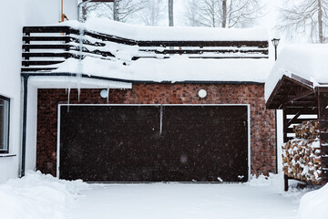Automatic garage door of a cottage in a snowfall. Winter house with automatic garage doors. Mansion...