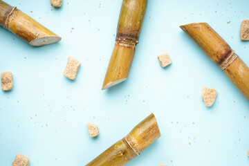 Sugar cane and brown sugar pieces on blue background, top view.