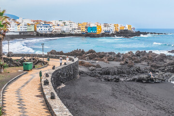 Fototapeta na wymiar Puerto de la Cruz, Spain - November 25, 2021: Promenade in Puerto de la Cruz. Atlantic Ocean coastline and empty Playa Chica beach with black sand during a storm