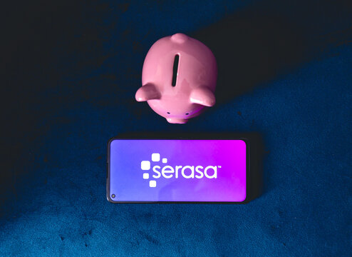 Serasa. Um telefone celular com a logo da empresa brasileira Serasa e um cofrinho sobre um sof&aacute; azul. Consulta, inadimpl&ecirc;ncia, consumidor, d&iacute;vida vencida, nome sujo, negativado, limpar o nome.