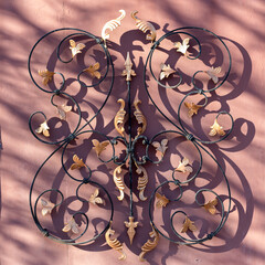 Floral ornament in arabesque style on metal gates, detail. On pink (powder-colored) background....