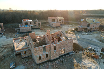 Fototapeta premium Aerial view of new homes with brick framework walls under construction in rural suburban area. Development of real estate in modern city suburbs