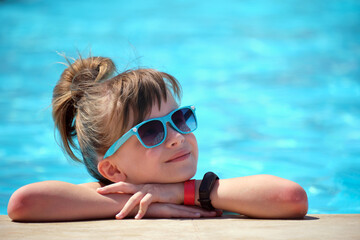 Happy child girl relaxing on swimming pool side on sunny summer day