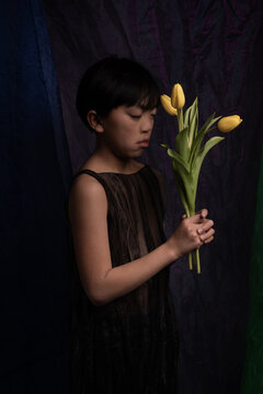 classic dark studio portrait of boy holding yellow tulip flowers